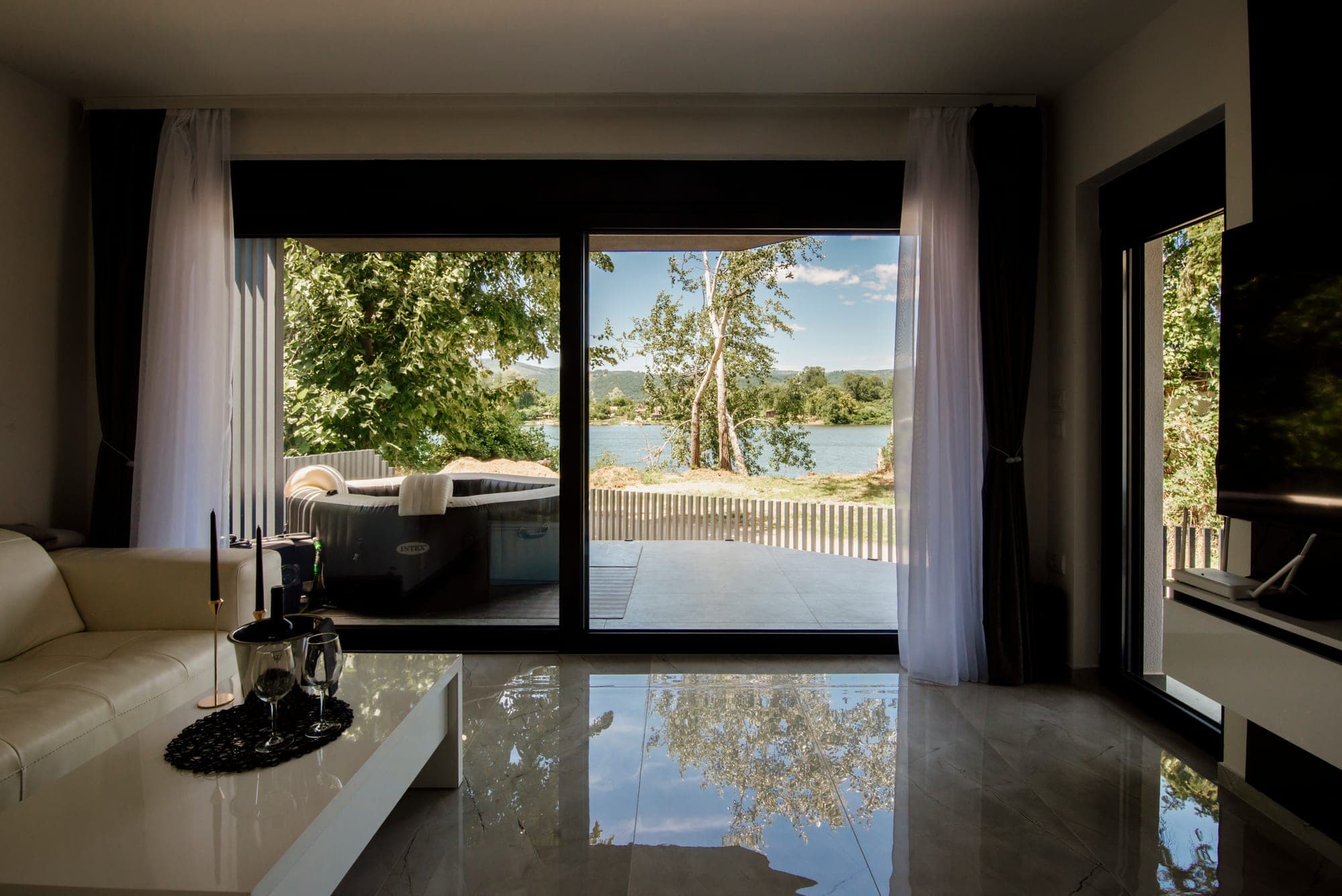 Modern living room with sheer drapery and a roller shade over a sliding glass door to a lake